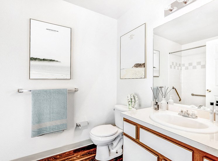Model Bathroom with White Counters, White Cabinets with Wood Accents and Towel Holder Under Framed Art